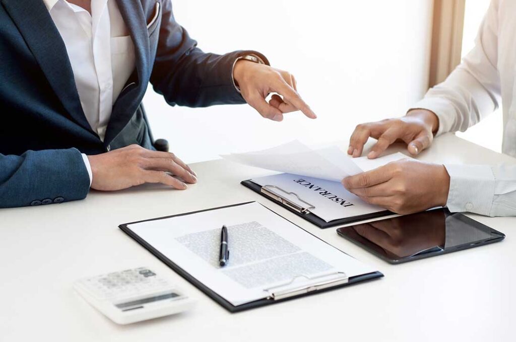 A homeowner carefully reviews jewelry appraisal documents and insurance papers at a kitchen table.